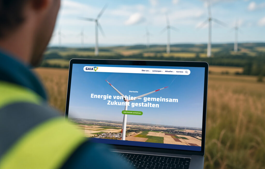 KI-generiertes hyperrealistisches Bild eines Mitarbeiters, der die GAIA-Website nach dem Markenrelaunch am Laptop betrachtet – mit Windmühlen im Hintergrund